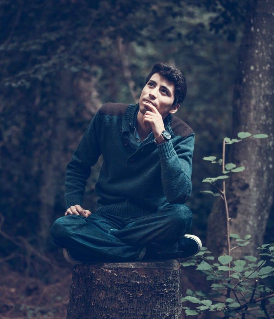 A man sitting on a stump in the woods.